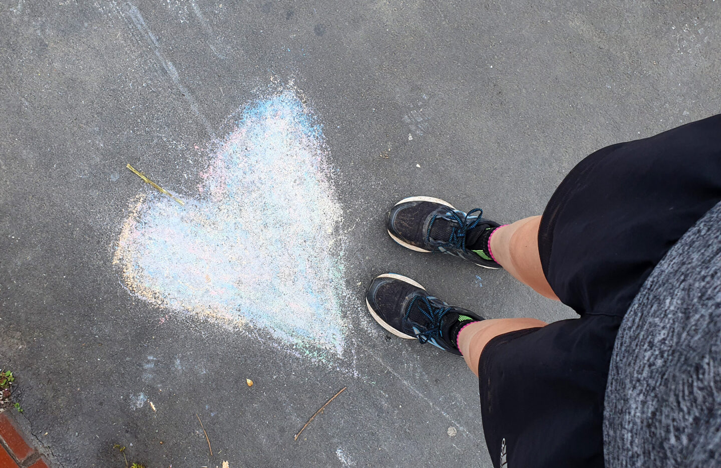 Girls legs stood next to a heart drawn in chalk on the pavement.