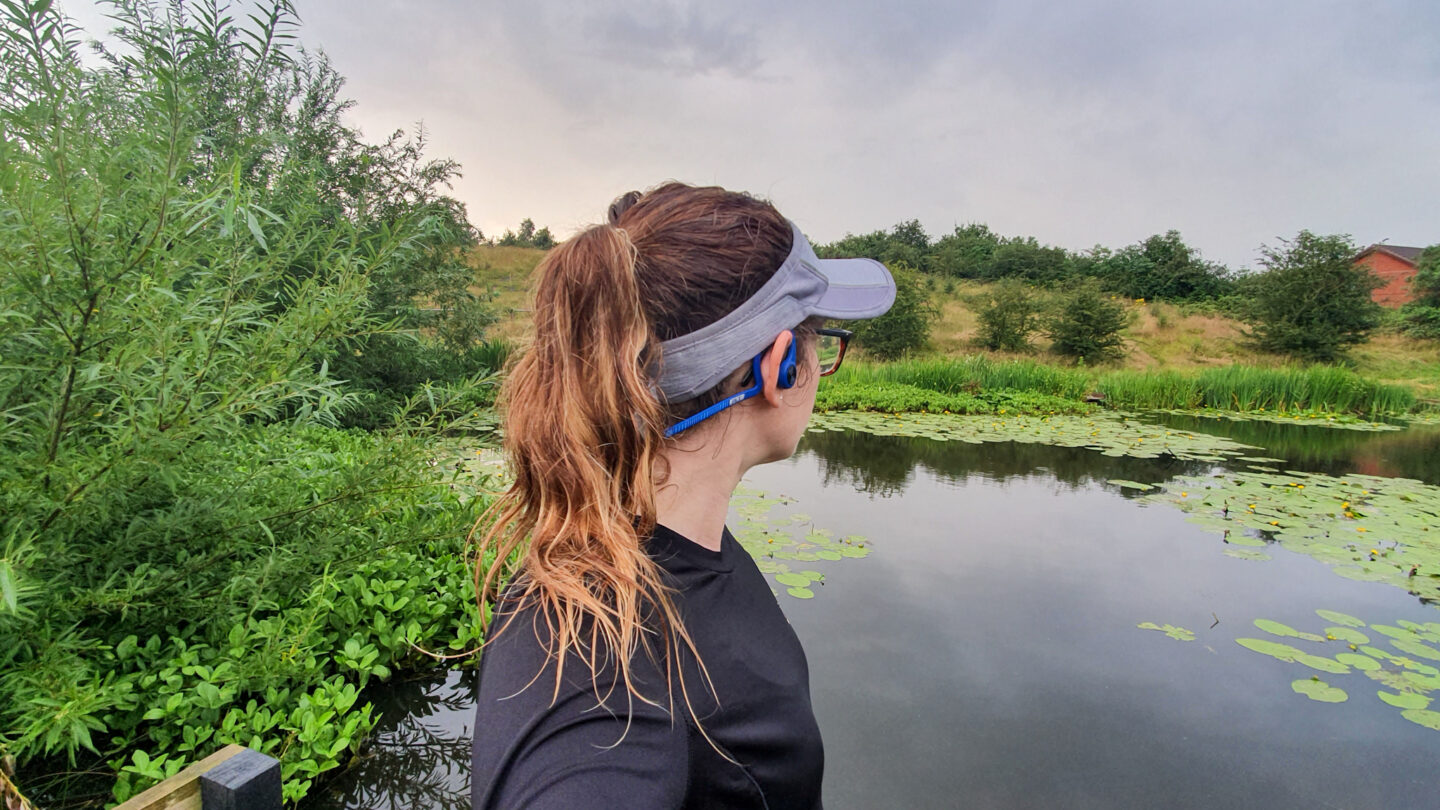 Photo of girl wearing visor and earphones with pond behind her | Marathon Training
