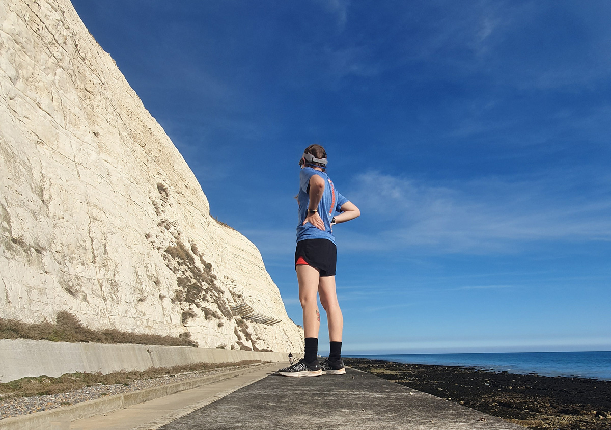 Girl stood on wall with white cliffs to left and blue skies to right,
