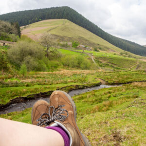 Legs wearing boots can be seen in the foreground, with a hill in the distance - hiking tips