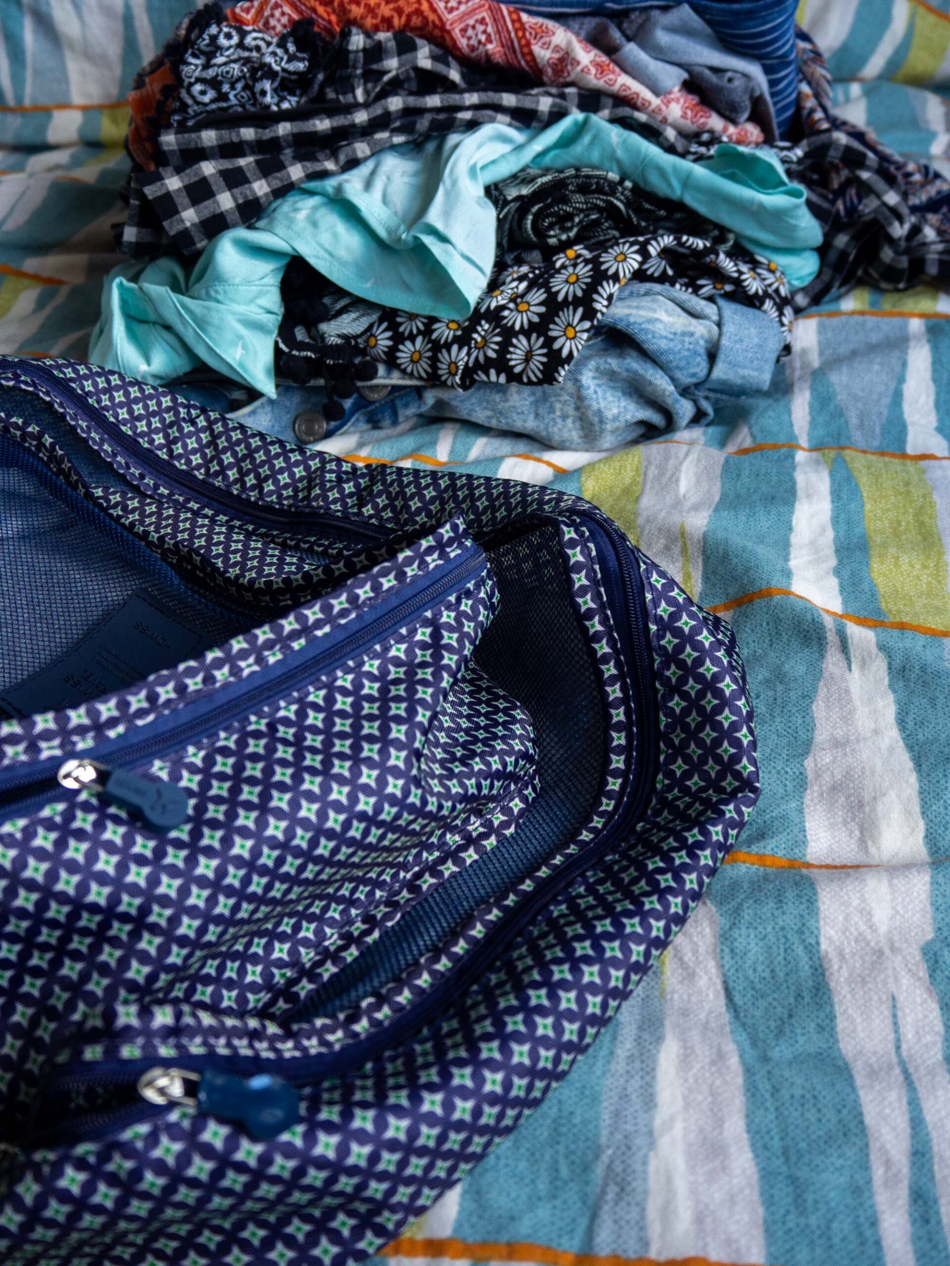 Packing cubes are on a bed, with a pile of clothes in the background.