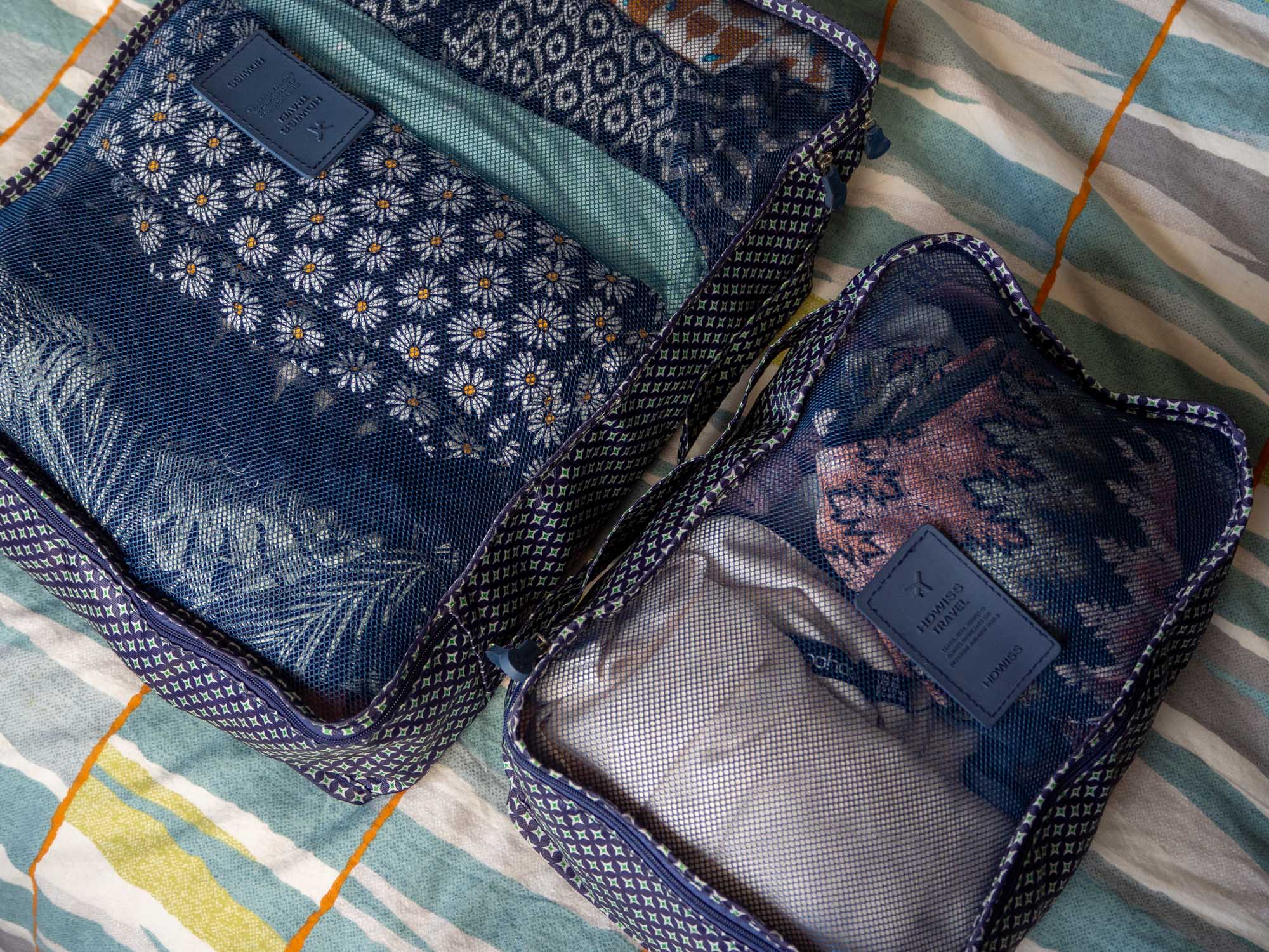 Two packing cubes are on a bed, filled with clothing.