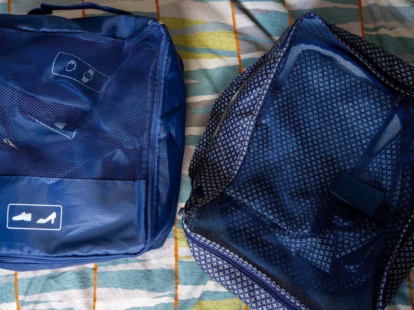 Travel packing cubes in two different designs. One set is plain navy blue, one set is navy blue with a diamond pattern.